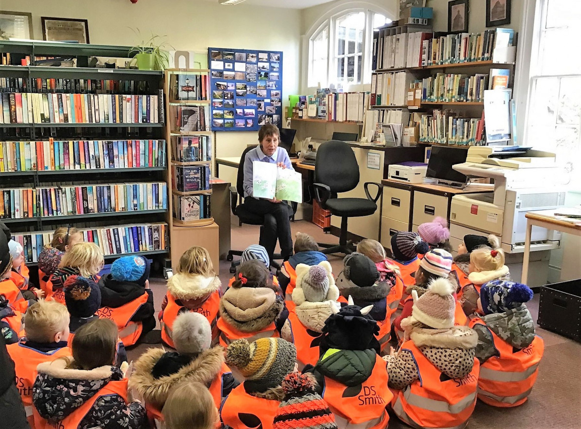 Picture of a woman reading a book to a class of children in a library
